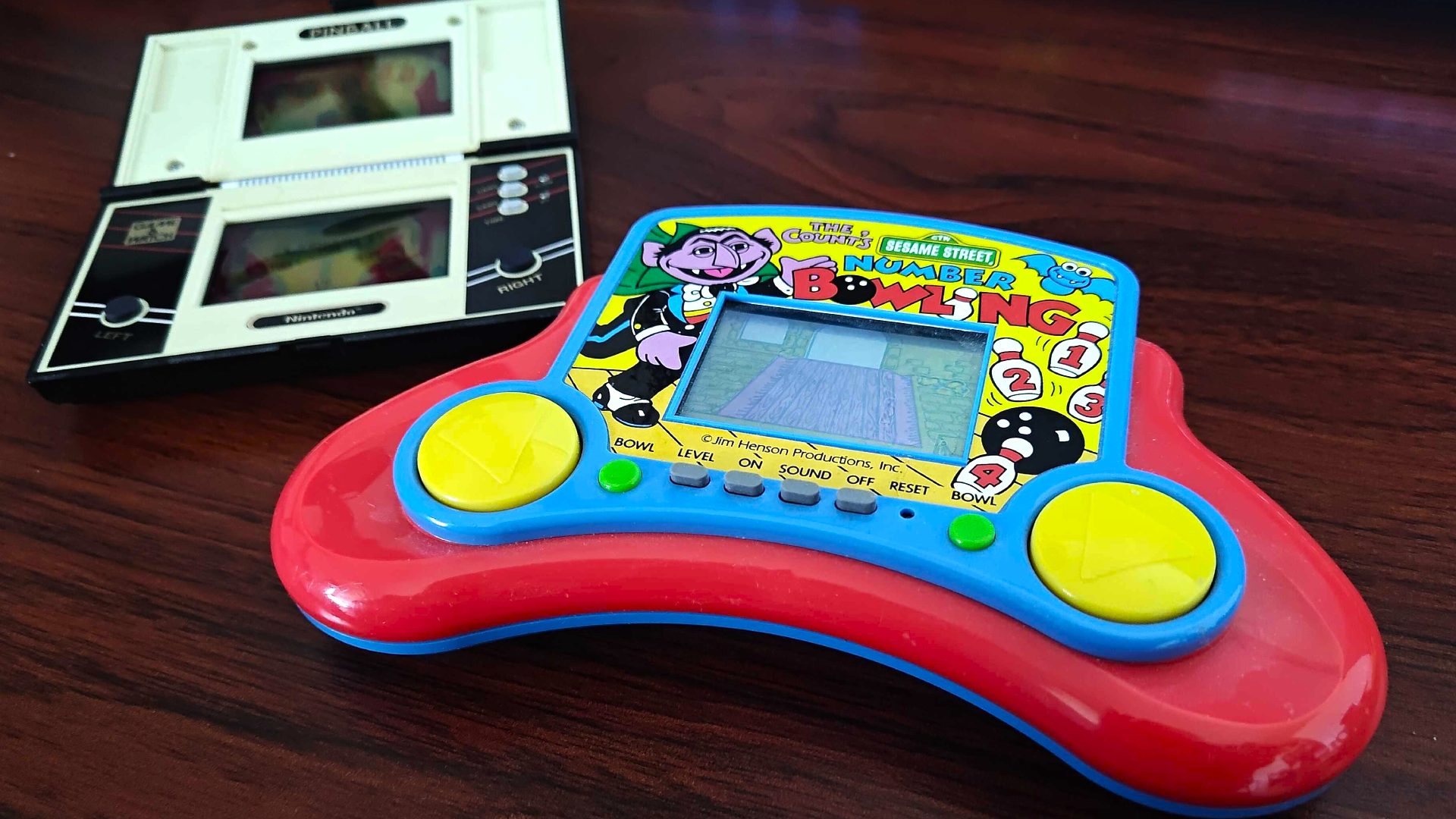Sesame Street Number Bowling LCD game next to Nintendo Game and Watch Pinball on woodgrain desk.