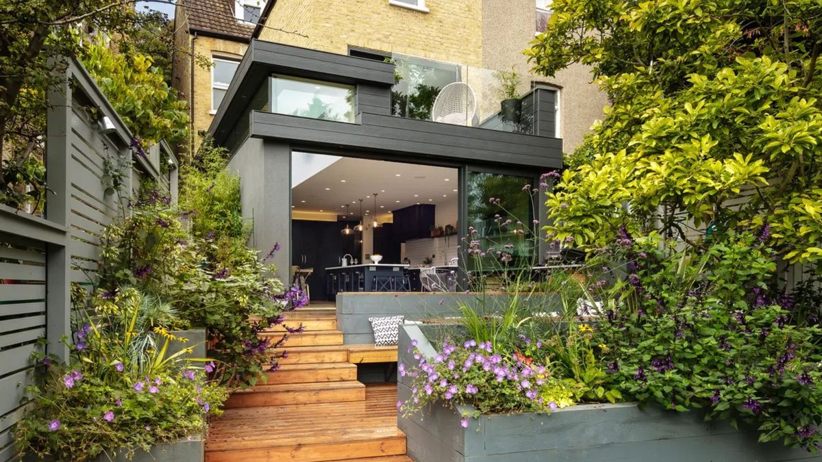 A contemporary rear extension with large glazed features and decking with steps leading to a garden below