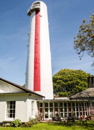 lighthouse in red and white colour near house with sloping roof top