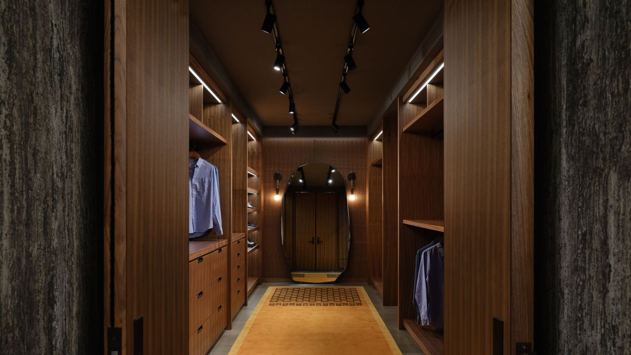 walk-in wardrobe with timber panelling, mustard yellow carpet, track lighting, mirror at the end of the closet