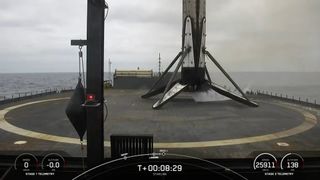 A black and white spacex falcon 9 rocket first stage sits on the deck of a ship at sea.