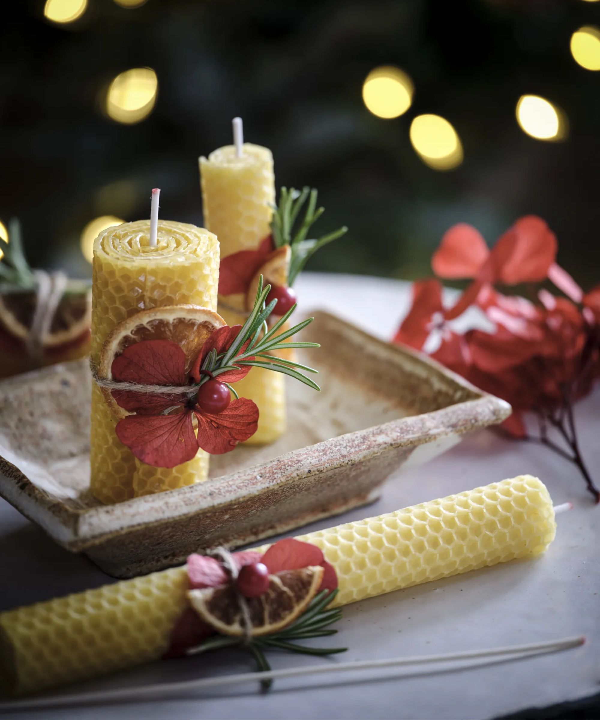 Beeswax candles decorated with berries, dried orange slices, and rosemary sprigs