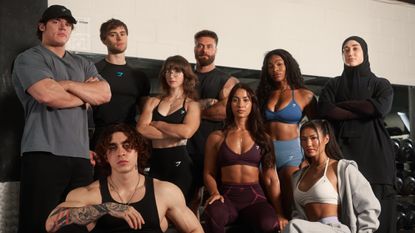 Nine Gymshark athletes pose wearing the brand's apparel. Behind them we see a dumbbell rack.