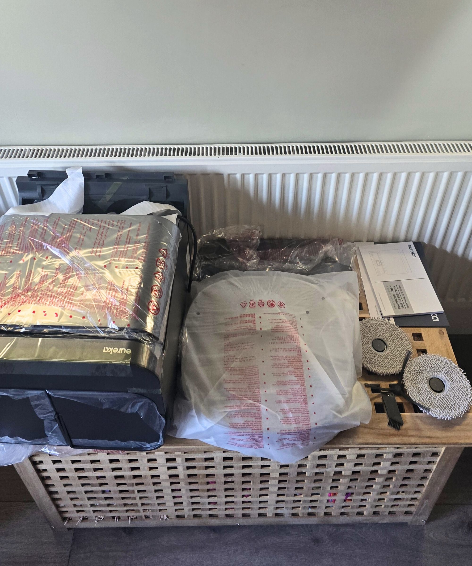 A birds eye view of packaged parts of a Eureka J15 Pro Ultra vacuum, with a white radiator behind them