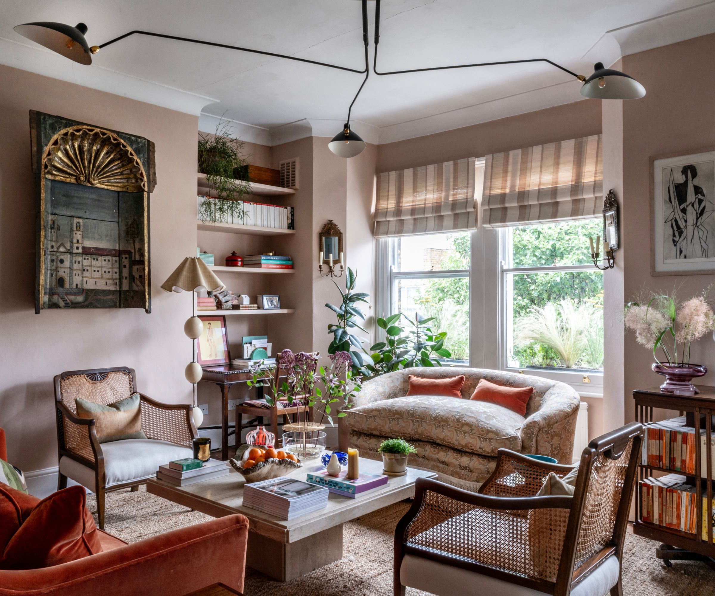 Transitional living room with pale pink walls, orange velvet sofa, midcentury pendant, antique art, marble coffee table with decor