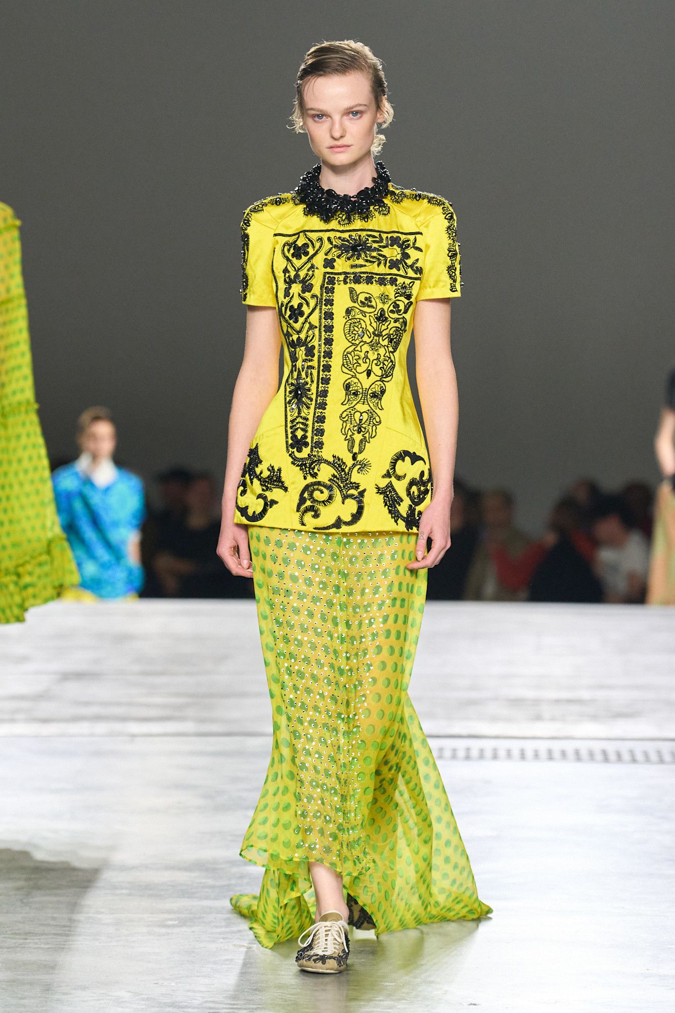 A model at the spring/summer 2026 Dries Van Noten show wearing a chartreuse beaded tunic with a polka dot sheer skirt and brocade-printed sneakers.
