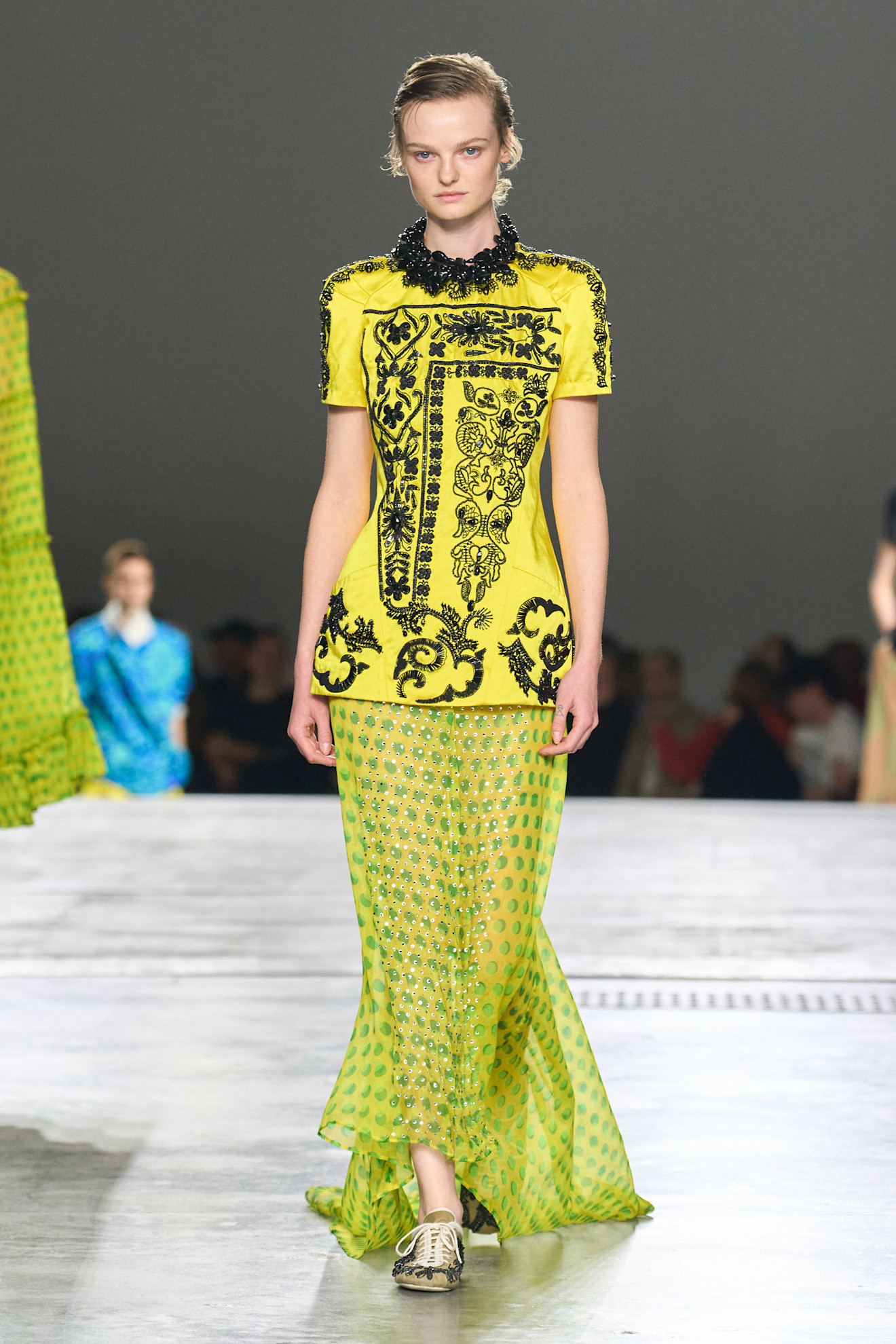 A model at the spring/summer 2026 Dries Van Noten show wearing a chartreuse beaded tunic with a polka dot sheer skirt and brocade-printed sneakers.