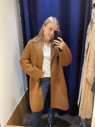 Woman wears camel coat, white t-shirt and blue jeans