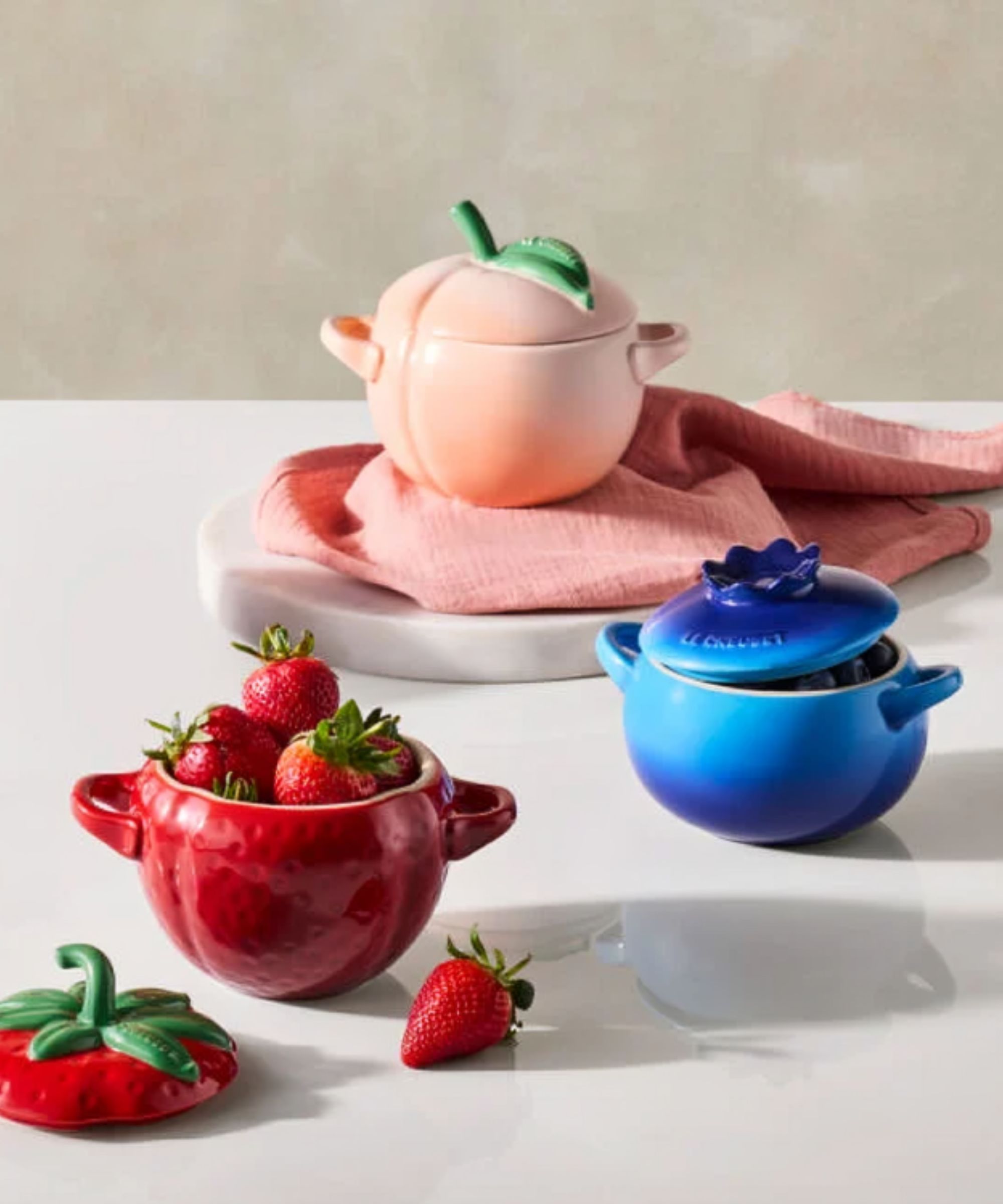 A set of three fruit shaped cocottes, in a peach, strawberry, and blueberry design