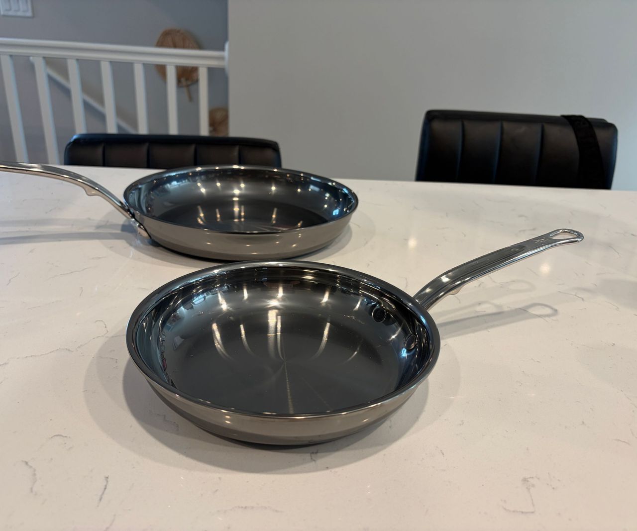 Two shiny frying pans viewed from above, on a white kitchen counter