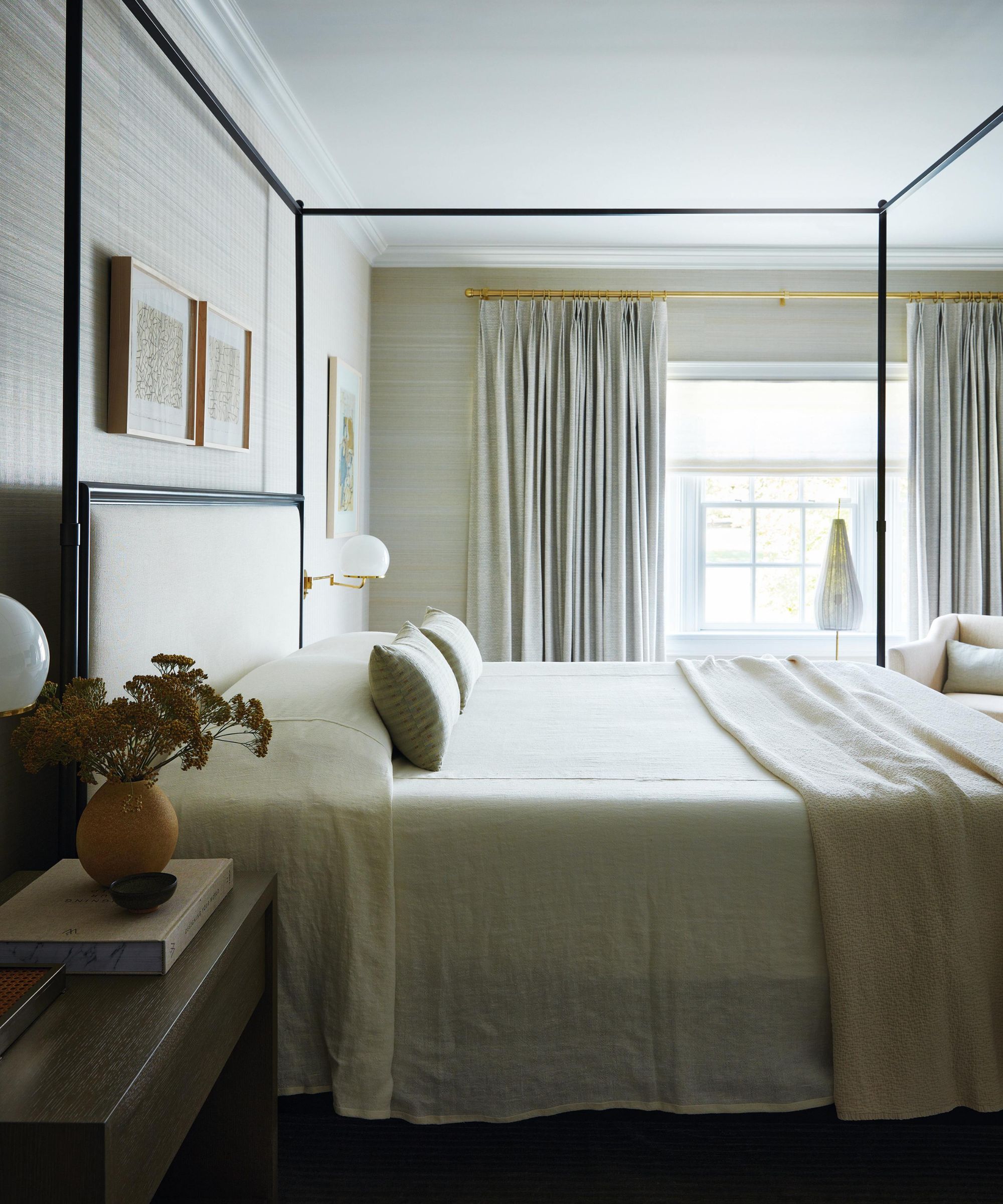 a neutral master bedroom with a black four posted bed with neutral bed linens and vintage style globe sconces