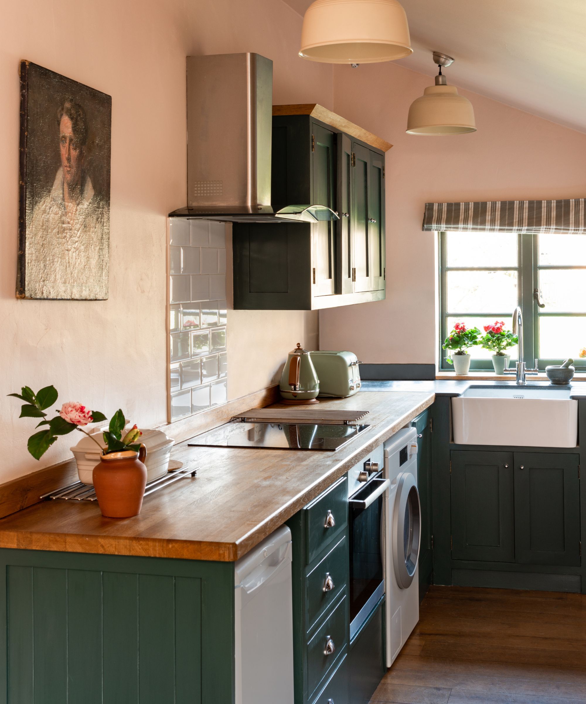 Kitchen with dark green painted cabinetry, pink walls, wood countertops and pendant lights