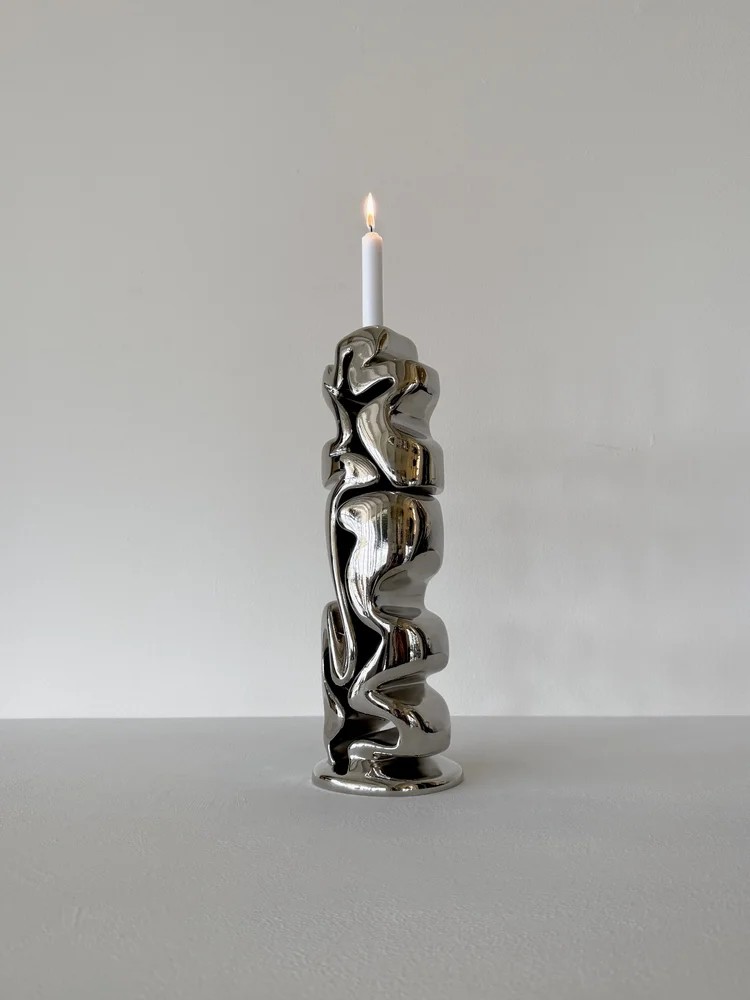 Image of an abstract chrome candle holder in front of a light gray background.