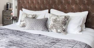 bed with gray velvet button headboard and a stack of pillowpillows