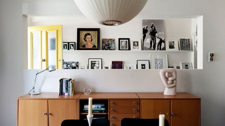 Entryway with a yellow front door, picture ledges along the wall with framed prints and photos, midcentury console, and a lantern pendant light