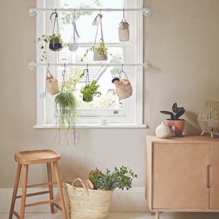 A living room with a light wooden sideboard and two rails with hanging plants across the window