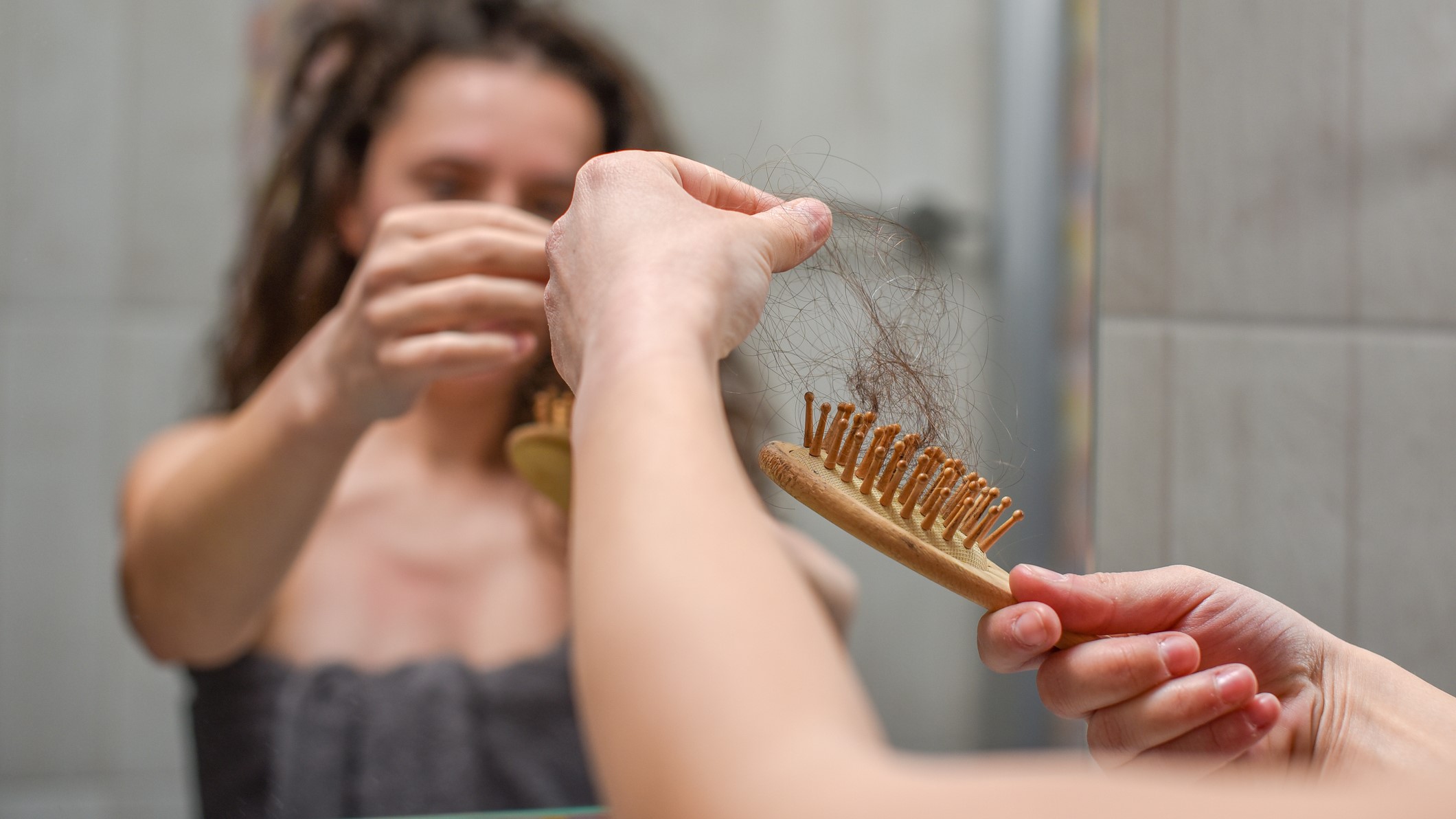 A person looking in the mirror and holding a brush with hair