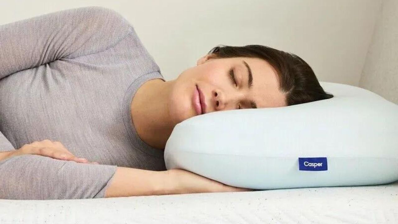 A dark haired lady closes her eyes as she lays her head on the Casper hybrid pillow with snow technology