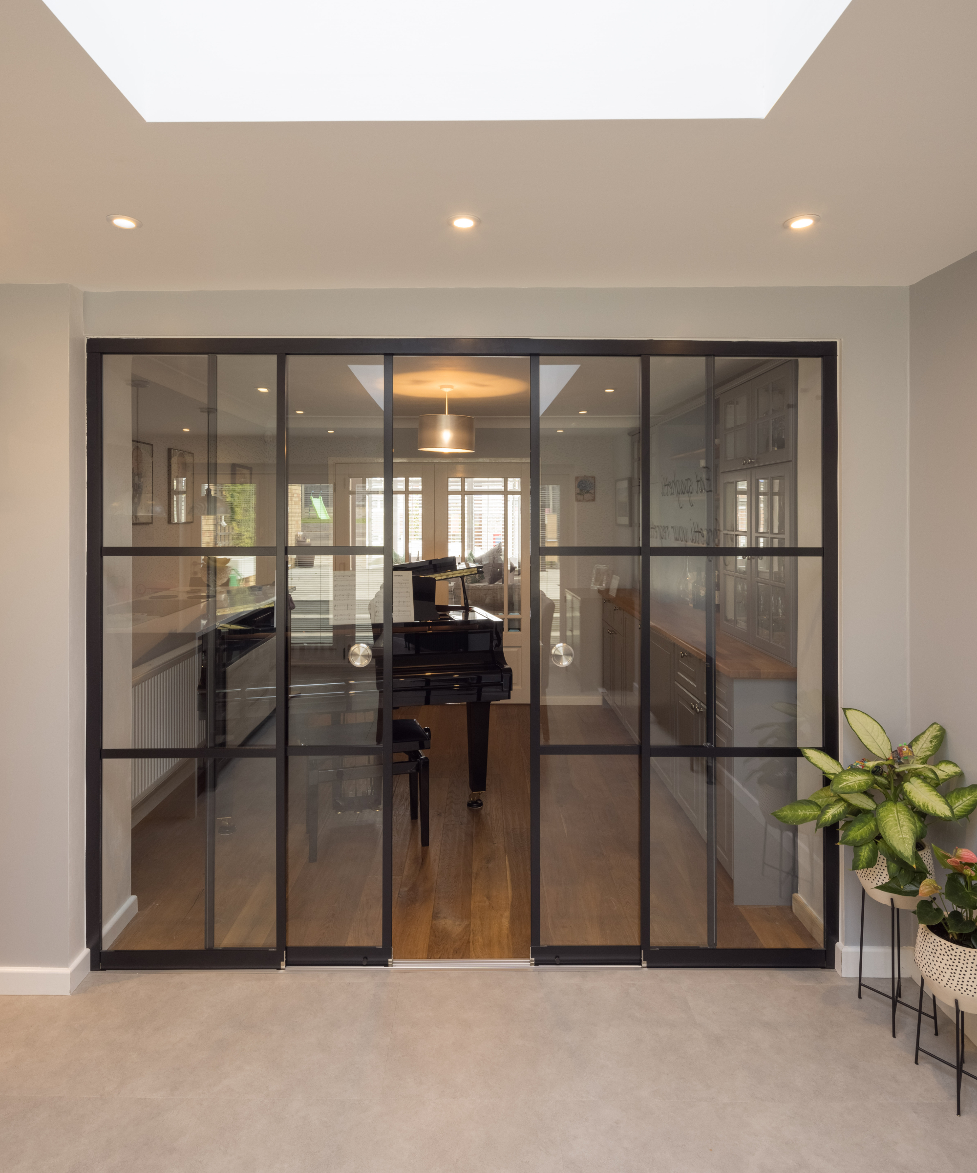 black framed glass doors leading to music room with piano and white doors at the end