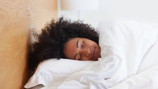 A woman sleeps wrapped in a blanket with her head flat on a pillow
