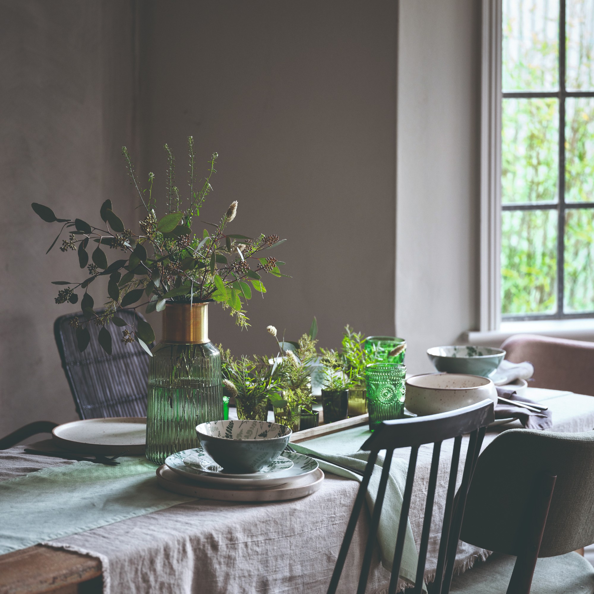 A grey-painted dining room with a rustic dining table, linen tablecloth and mismatched chairs
