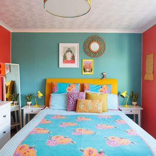 bedroom with multicolour wall and bedside table with yellow lamps and bedding with multicolour cushions and throw