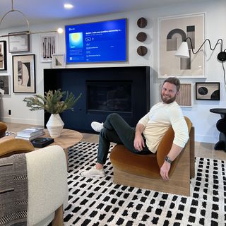Bobby Berk sat on armchair in living room with TV on wall.