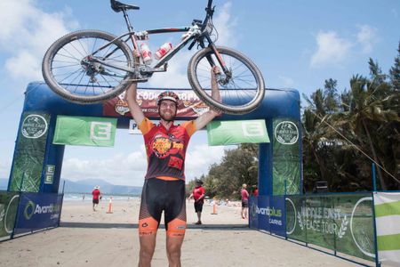 Leandre Bouchard - lifting his bike at the finish line at Port Douglas as the Crocodile Trophy Champion