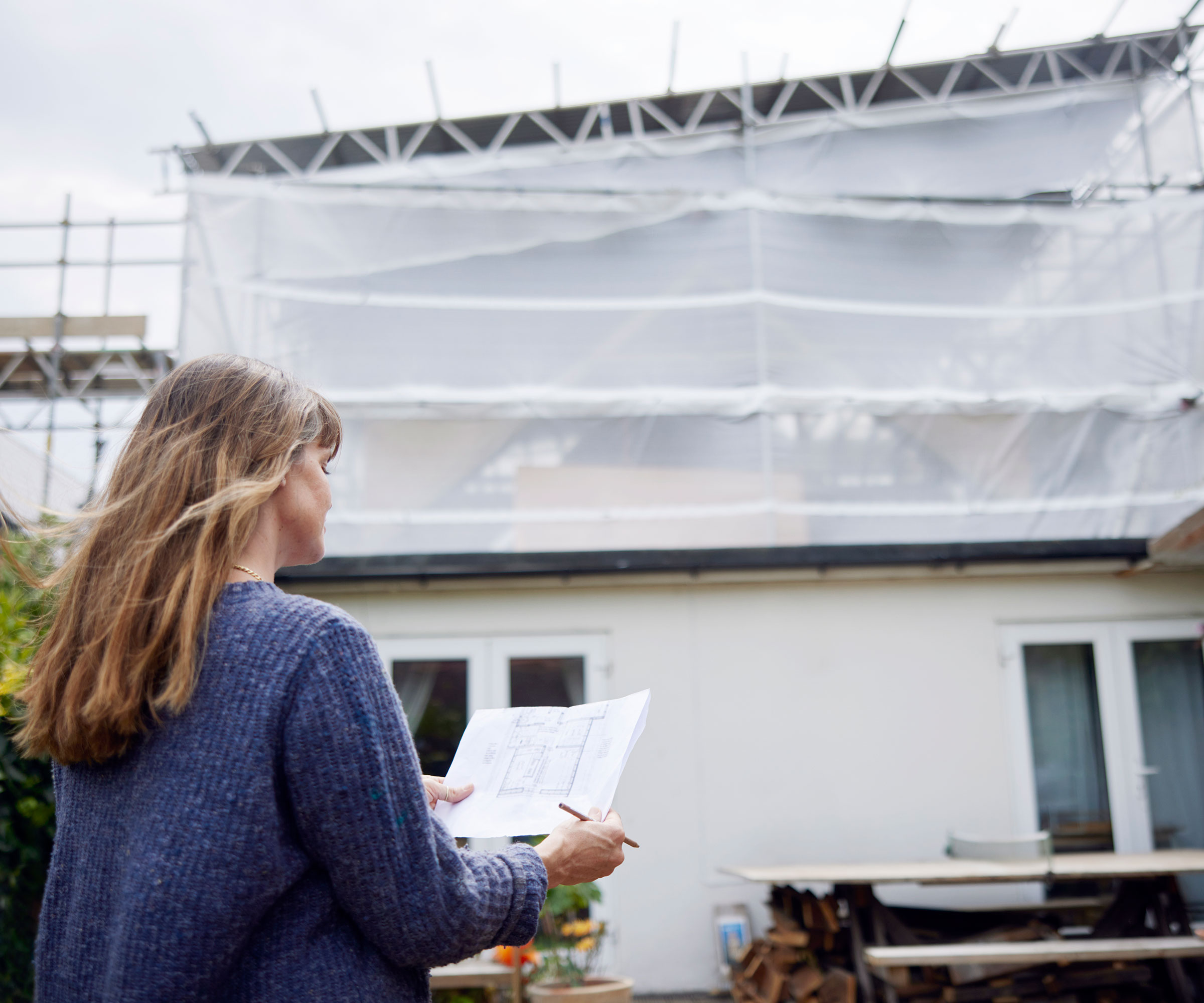 woman looking at architectural drawings in front of a house covered in scaffolding
