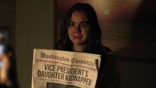 Sarah Desjardins holding up a newspaper in a dimly lit room as proof of life in The Night Agent.