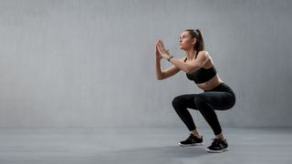 Woman performing a squat against grey backdrop
