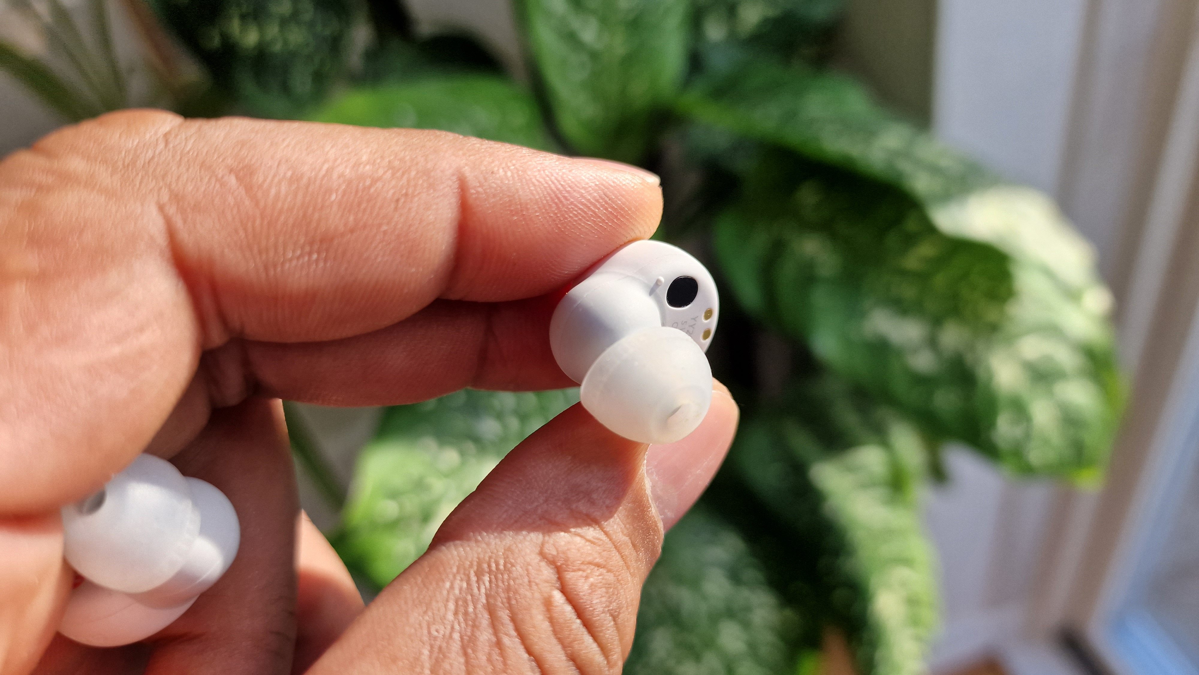 Sony LinkBuds S hold imellem tommel og pegefinger foran en grøn plante.