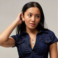 Young woman putting hair behind her ear, wearing denim shirt and silver pearl necklace.