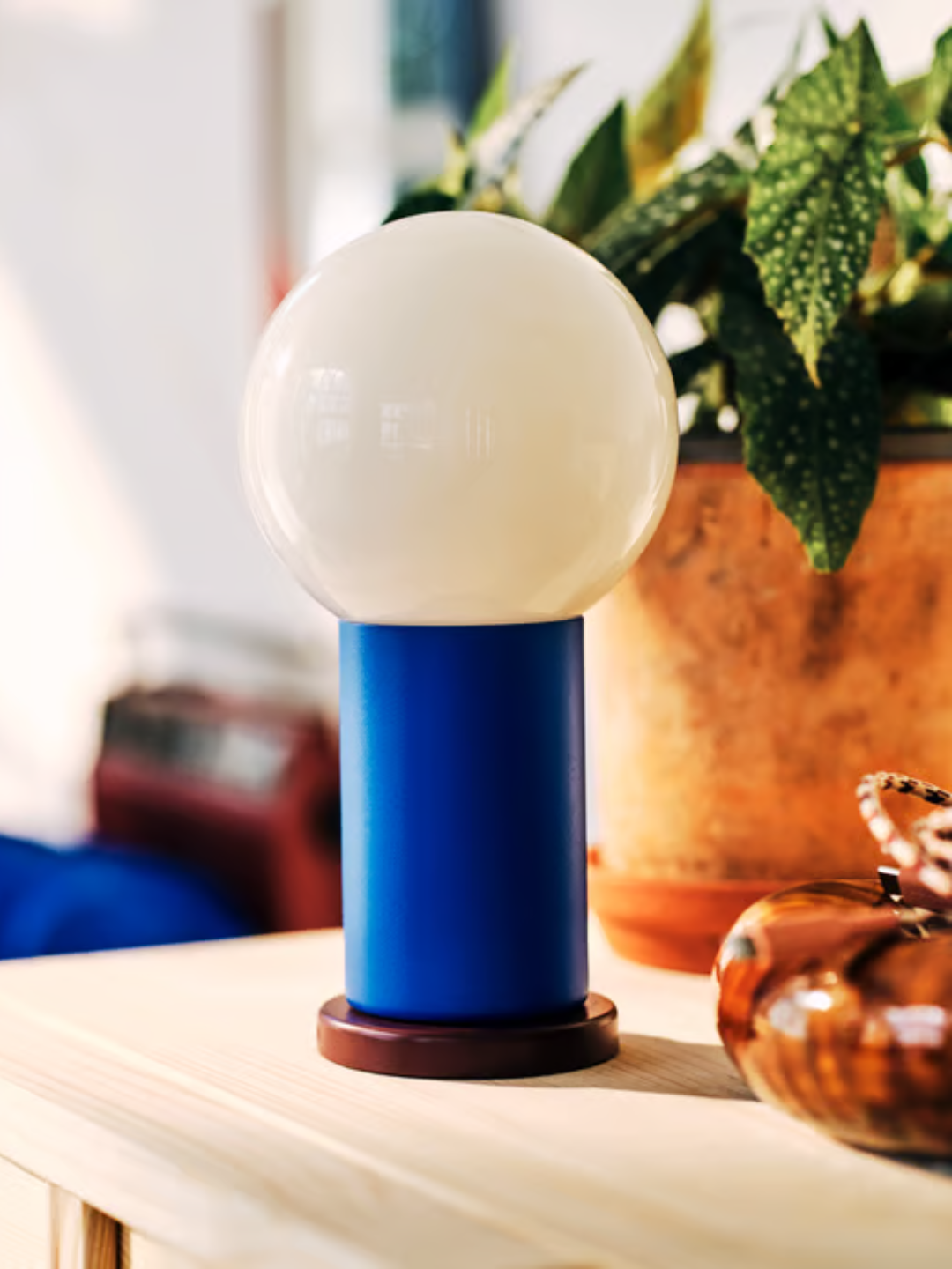 A portable lamp from IKEA with a burgundy base, a cobalt blue stem, and a round bulb