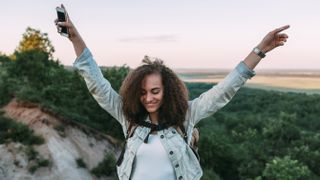 Happy teenage girl with smartphone and backpack in nature