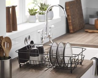 simplywire Black Dish Drainer with Cutlery Basket in white and wooden kitchen beside sink with large tap, filled with plates, mugs and cutlery