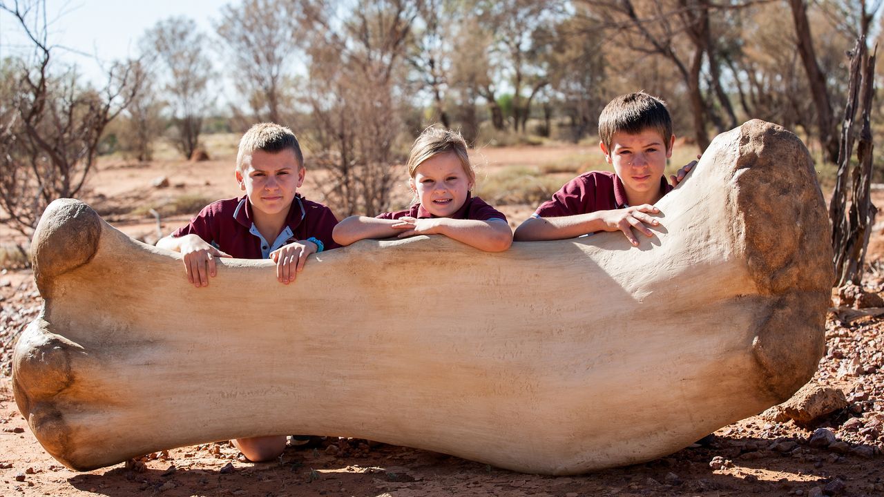 Students from Eromanga State School size up against a replica of Cooper's femur (thigh bone) at the Eromanga Natural History Museum.