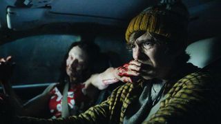 Austin Abrams in a car while a bloody zombie covers his mouth with one hand