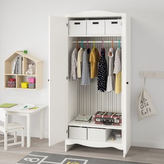 white nursery with white free-standing wardrobe, desk and chair, wall mounted shelving and peg rail