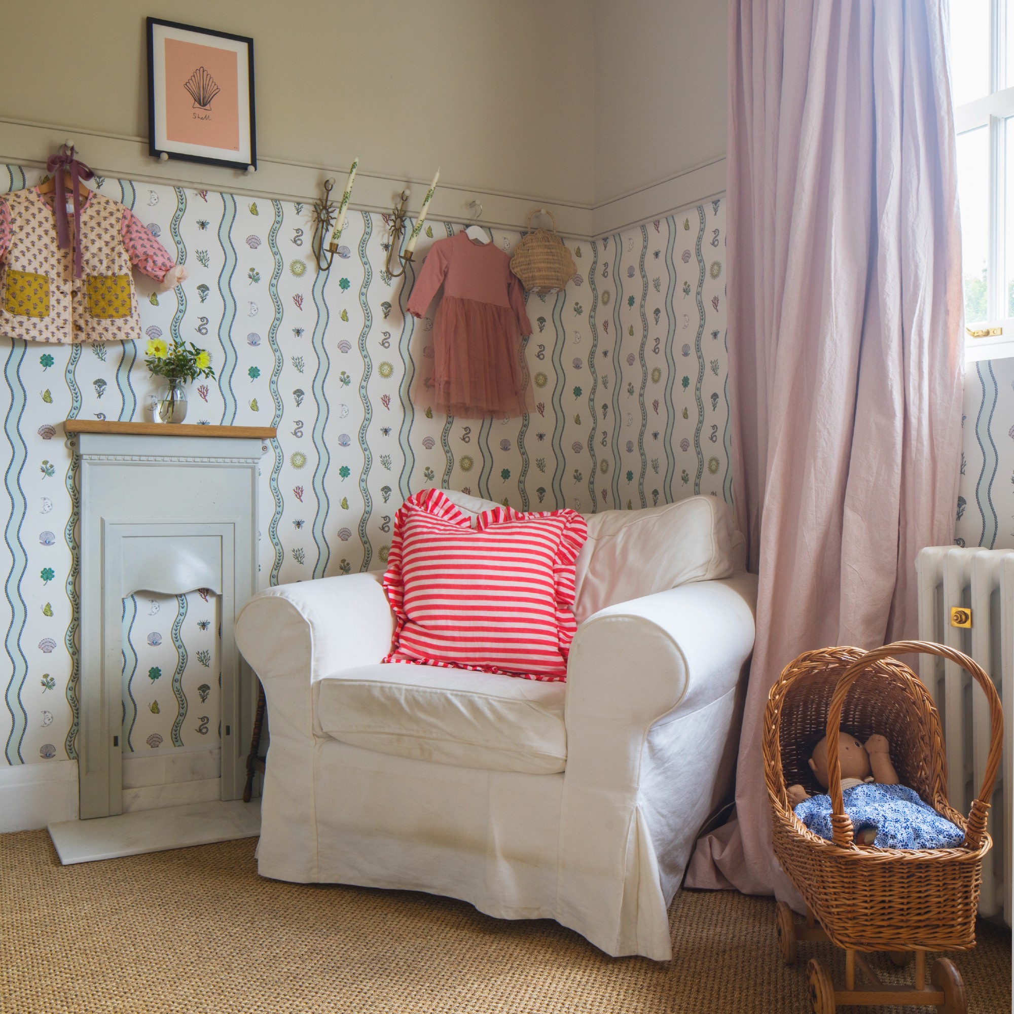 A nursery with half wallpaper-covered walls and a white armchair in the corner