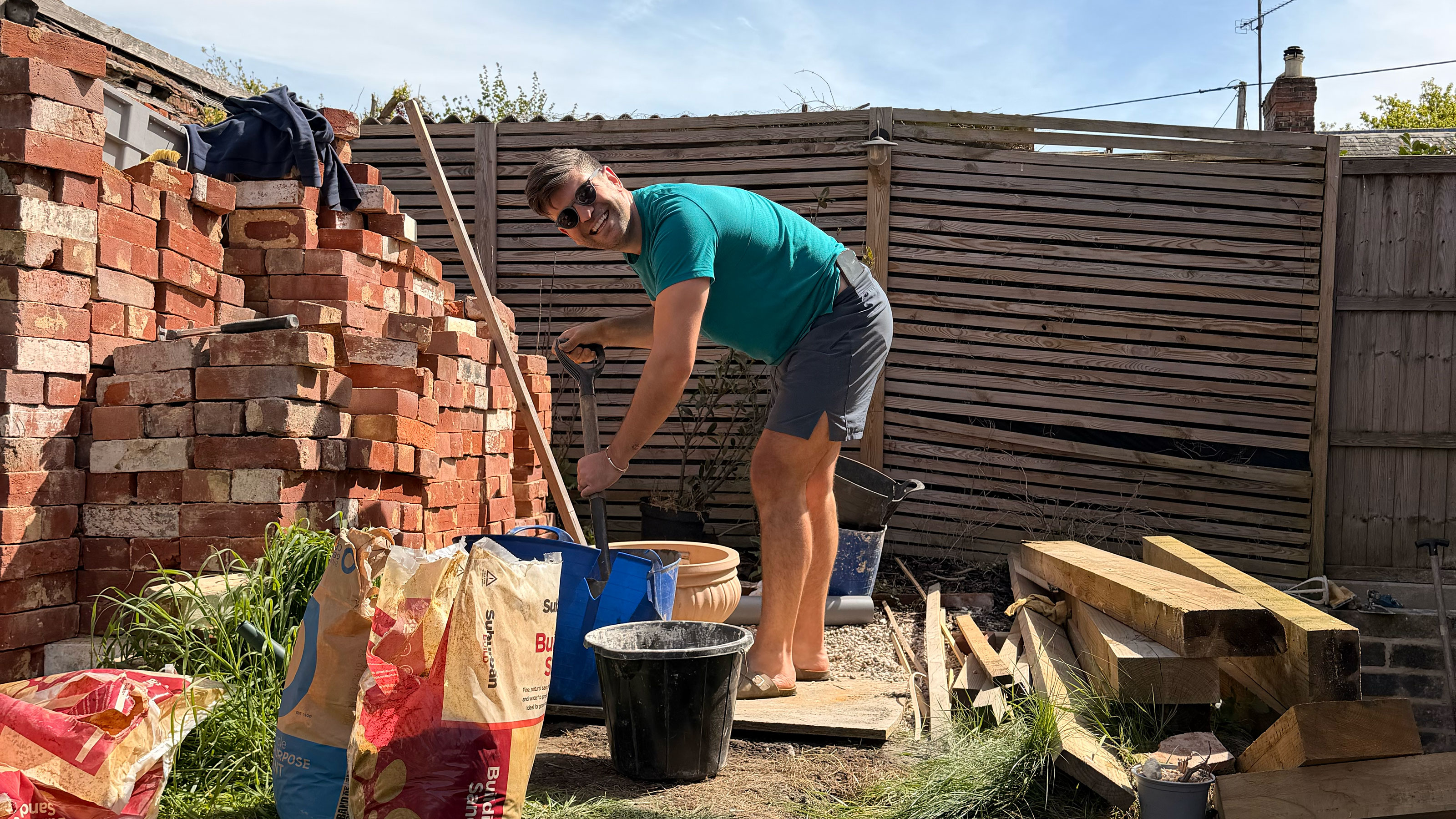 Man in garden by wooden fence and large pile of bricks