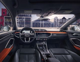 Audi Q3 photographer from the inside. All black leather with orange details. Through the windshield, we see buildings in the distance.