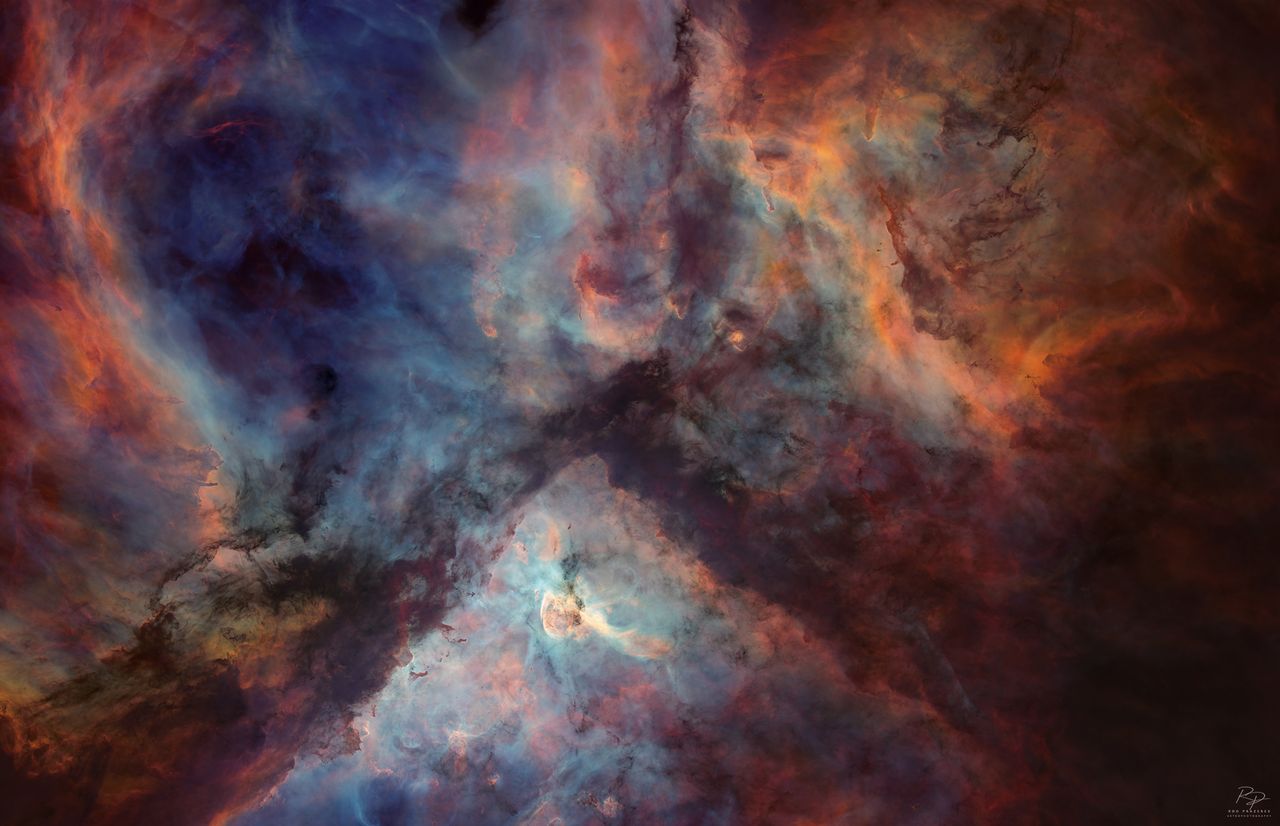 A deep space nebula scene is shown, featuring swirling masses of colorful interstellar gas and dense, dark dust filaments.
