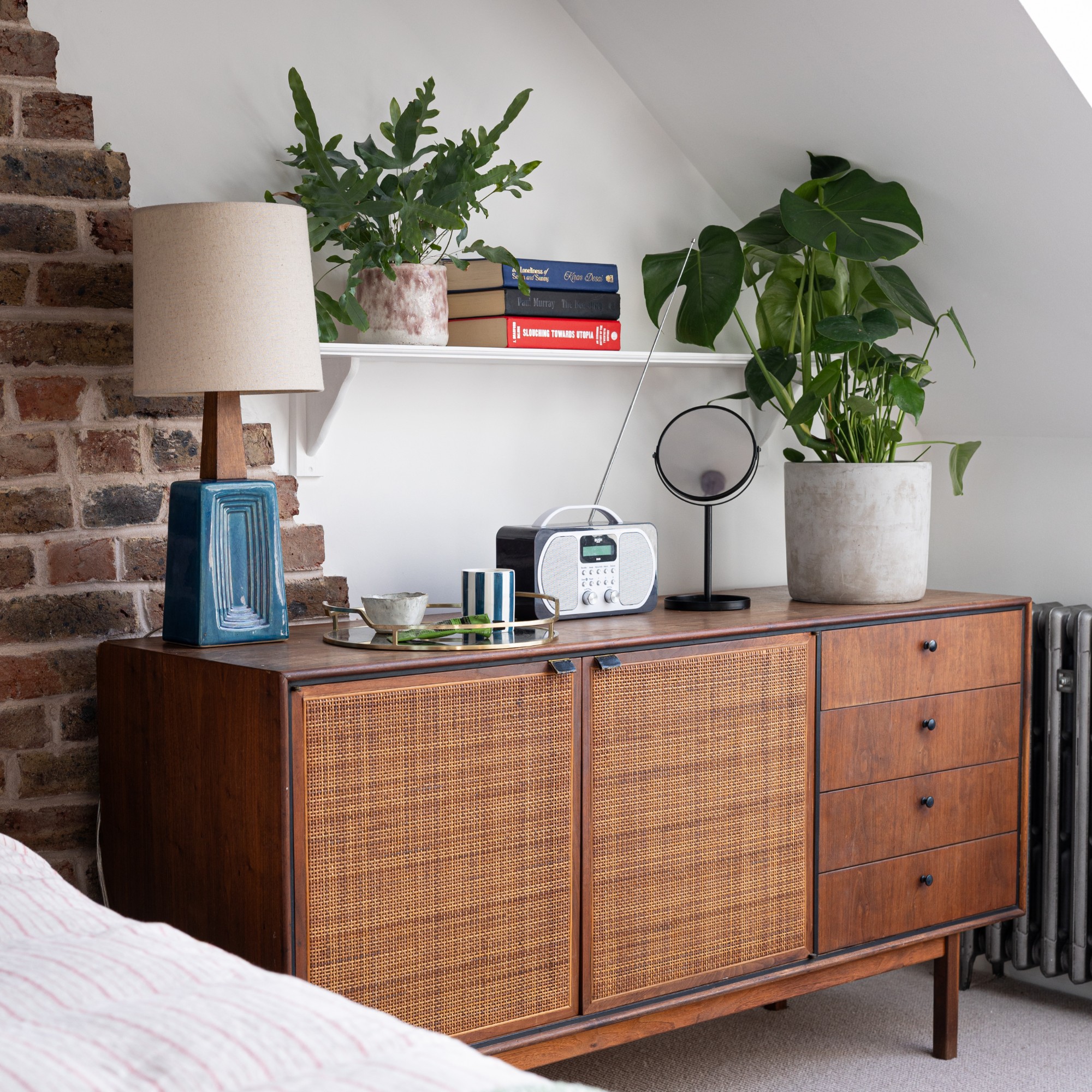 A white bedroom with a vintage wooden sideboard used instead of a bedside table
