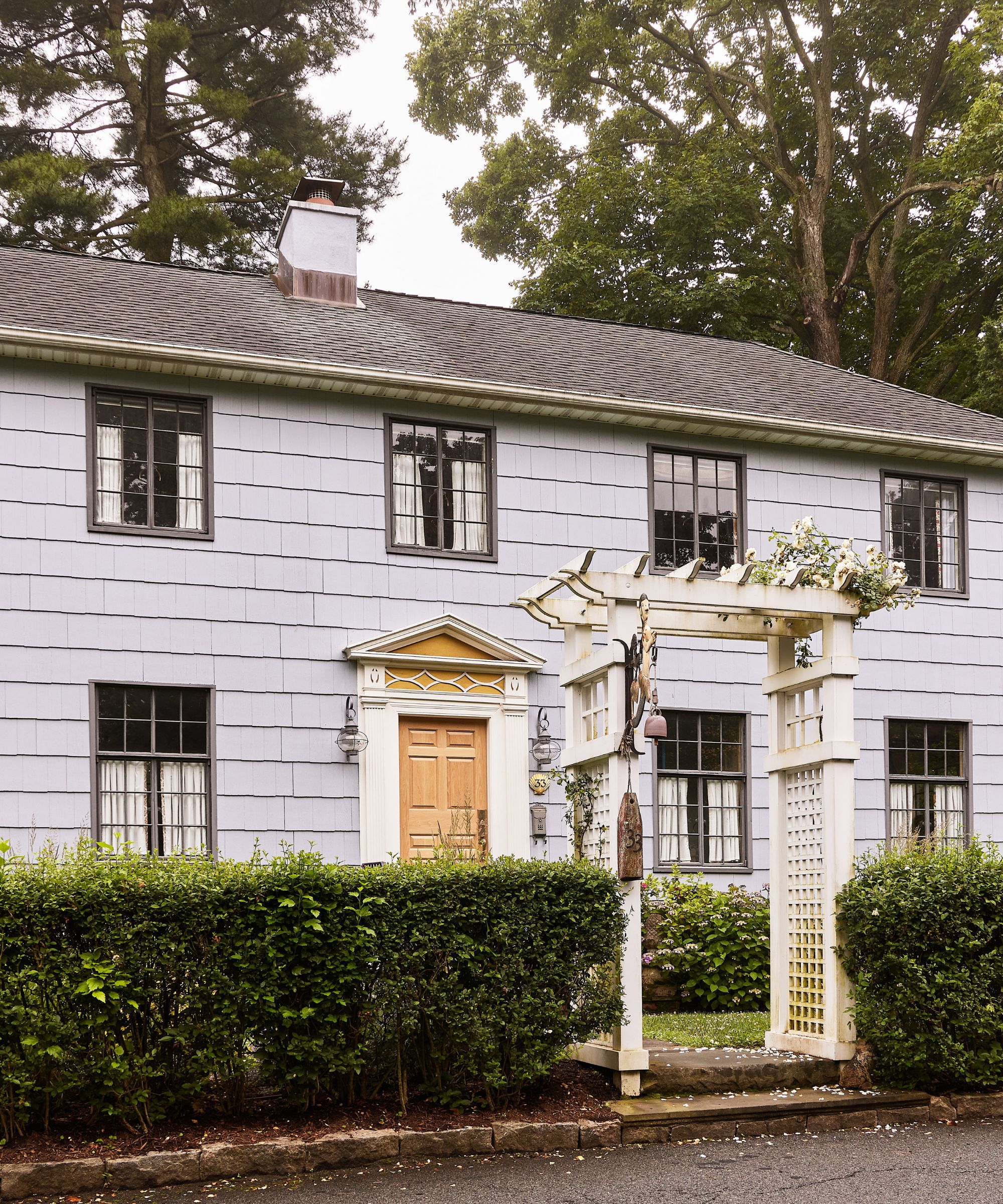 a bungalow in New Rochelle, Westchester New York with white cladding, a wooden front door, traditional windows, and a hedged front yard with white pergola