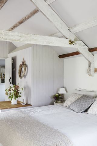 bedroom in converted barn with white painted rafters and tongue and groove paneling