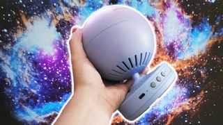 Pococo Galaxy star projector in the hand with a nebula projection in the background