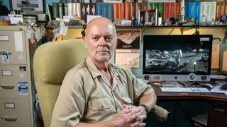 a man in a button-down shirt poses for a portrait in a room full of books