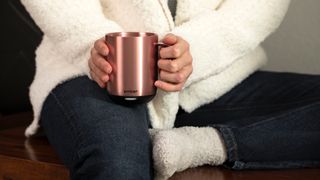 A woman holding a copper Ember Smart Mug 2. She is wearing a white fluffy cardigan and dark blue denim jeans.