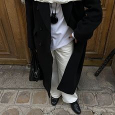 A woman wears smooth leather loafers with white pants and a black overcoat